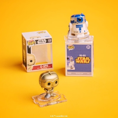 Duas figuras Funko Pop Star Wars R2-D2 azul e branco e C-3PO dourado sobre fundo amarelo