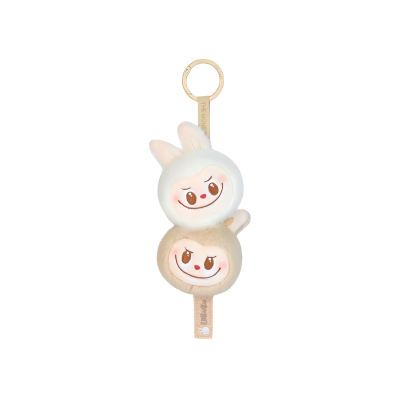 Chaveiro com duas figuras redondas sorridentes, uma branca com orelhas de coelho e outra bege, penduradas numa argola metálica dourada.
