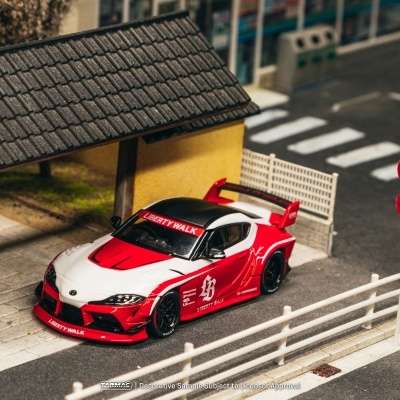 Miniatura de carro desportivo vermelho e branco estacionado junto a construção amarela e estrada