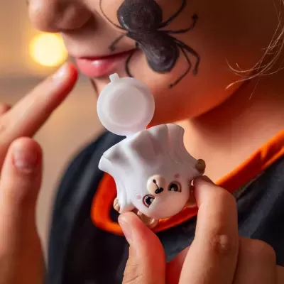 Dispensador de creme em forma de esquilo branco com rosto simpático perto do rosto de uma criança com aranha pintada.
