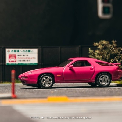 Carro desportivo rosa numa rua com sinalização e vegetação ao fundo