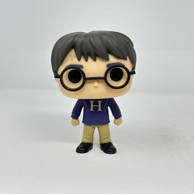 Figura colecionável Funko Pop de personagem com cabelo castanho, óculos redondos, camisola azul com letra H e calças bege.