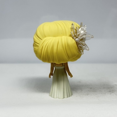 Figura boneca com cabelo amarelo e vestido branco vista de costas