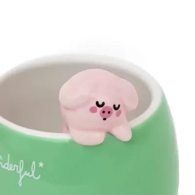 Caneca verde com figura rosa de porco na borda e texto parcial