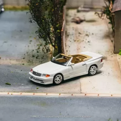 Miniatura de carro descapotável branco com interior bege numa estrada de asfalto perto de arbustos e prédio