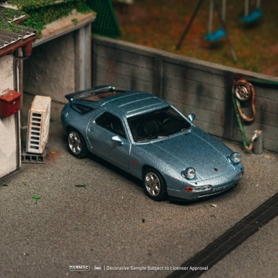 Miniatura de carro desportivo azul metálico num pátio com muro e porta aberta