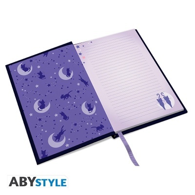 Caderno aberto roxo com ilustrações de gatos, estrelas e luas, folhas pautadas e fita marcador de página.