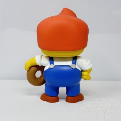 Brinquedo em plástico com gorro laranja e calças azuis a segurar um donut.