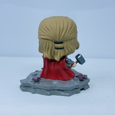 Figurinha de vinil de costas com capa vermelha e martelo sobre base cinzenta