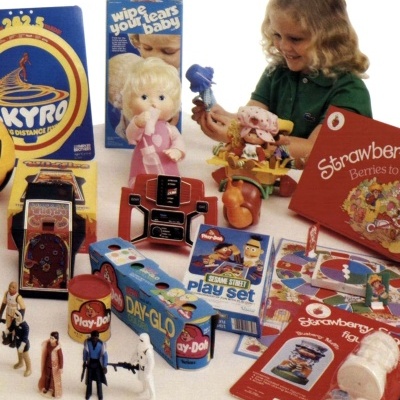 Brinquedos vintage e uma criança loira a brincar numa mesa com vários jogos infantis coloridos.