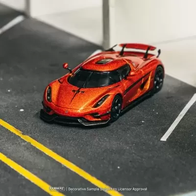 Carro desportivo miniatura laranja metálico com detalhes pretos num parque de estacionamento em miniatura
