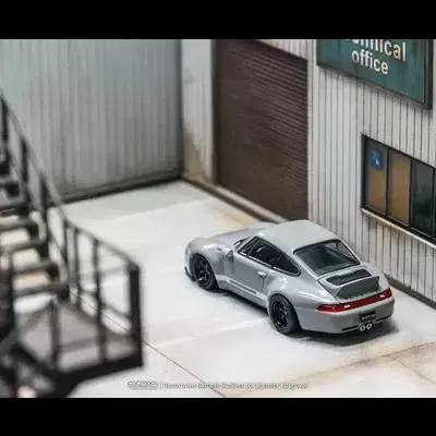 Modelo de carro desportivo prateado numa garagem ao lado de edifício industrial