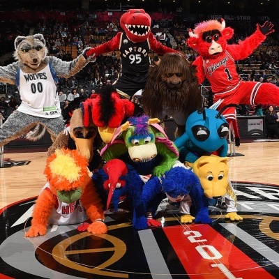 Nove mascotes de basquetebol com roupas coloridas numa quadra interior