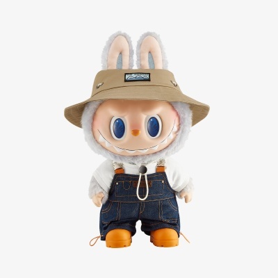 Boneco de pelúcia sorridente com chapéu bege e jardineiras de ganga