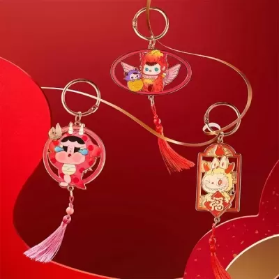 Três porta-chaves com personagens coloridos e franjas vermelhas e rosas sobre fundo vermelho.