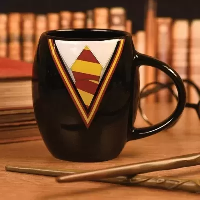 Caneca preta com padrão triangular vermelho, amarelo e branco numa mesa de madeira com livros ao fundo