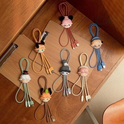 Carregadores USB com suportes de personagens em cores variadas sobre mesa de madeira