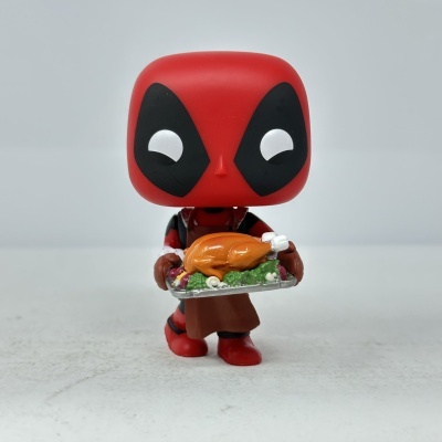 Funko Pop Deadpool com avental segurando tabuleiro com frango assado e legumes