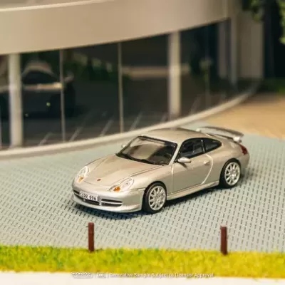 Miniatura de carro desportivo prata num cenário de miniatura com piso de calçada e edifício de vidro