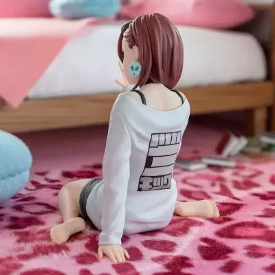Figura decorativa de personagem sentada com camisa branca e brincos azuis num tapete rosa com corações vermelhos
