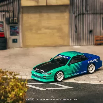 Carro de modelo em miniatura azul e verde com logótipos Falken junto a ambiente industrial
