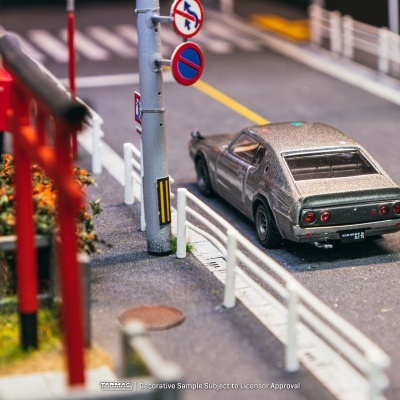 Carro de modelo em escala cinzento metálico numa estrada com sinais de trânsito.