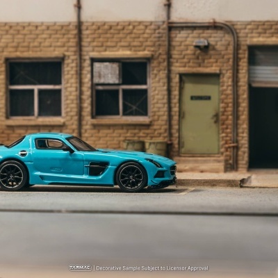 Miniatura de carro desportivo azul metálico em rua com parede de tijolos, janelas e porta verde.