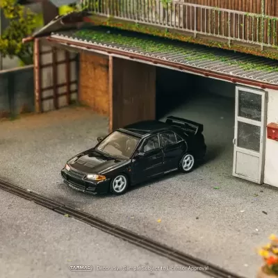 Modelo de carro preto estacionado em frente a garagem com parede branca e vegetação