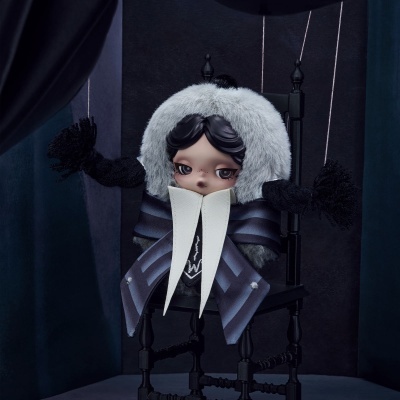 Boneca marioneta com capuz peludo sentada numa cadeira preta