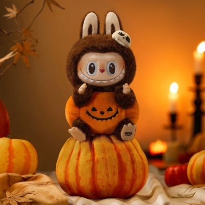 Figura decorativa com corpo de pelúcia e rosto de brinquedo entre abóboras e velas acesas