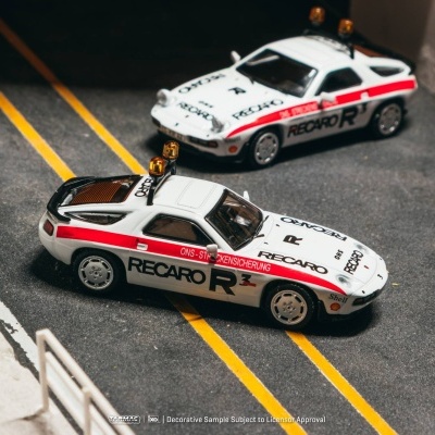 Dois carros de brinquedo brancos decorados com faixas vermelhas e texto preto em pista asphaltada.