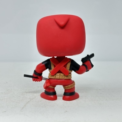 Figura Funko Pop de personagem de costas em roupa vermelha e preta com acessórios castanhos.