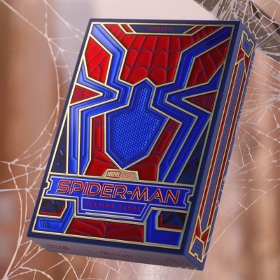 Caixa de baralho Spider-Man vermelho, azul e dourado sobre teia de aranha branca