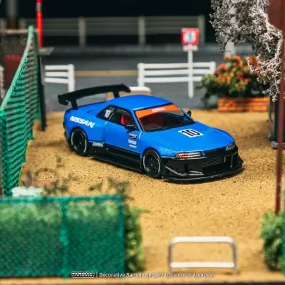Miniatura de carro desportivo azul NISSAN com número 10 junto a cerca verde e árvores em flor
