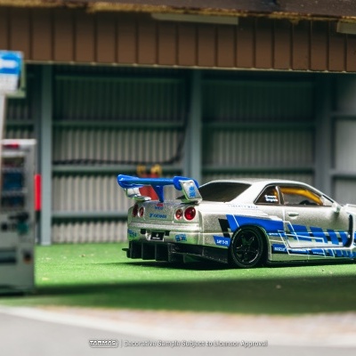 Carro de modelo em miniatura prateado com detalhes azuis e spoiler azul em parque de estacionamento simulado