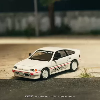 Miniatura de carro branco com letras pretas e vermelhas, placa japonesa, estacionado junto a poste em zona urbana