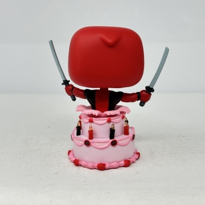 Figura de Deadpool a segurar duas espadas em cima de um bolo rosa com velas