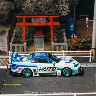 Carro de corrida em miniatura azul e branco numa estrada em miniatura com uma porta torii vermelha ao fundo