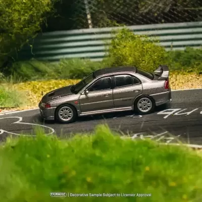 Maqueta de carro cinza numa pista de corrida com vegetação e marcações brancas.
