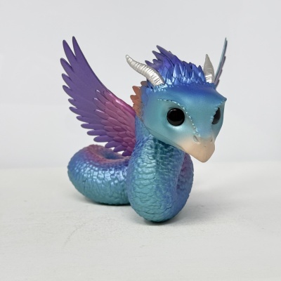 Figura de dragão azul com asas roxas e rosa em superfície branca