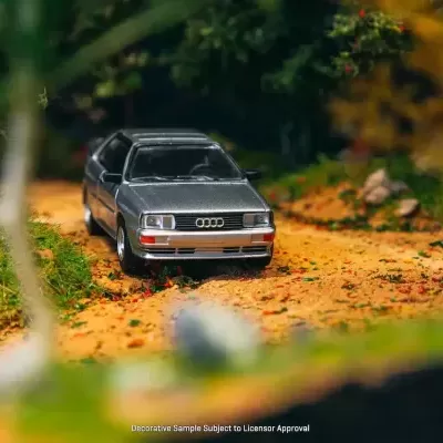 Miniatura carro Audi cinzento numa estrada de terra com vegetação