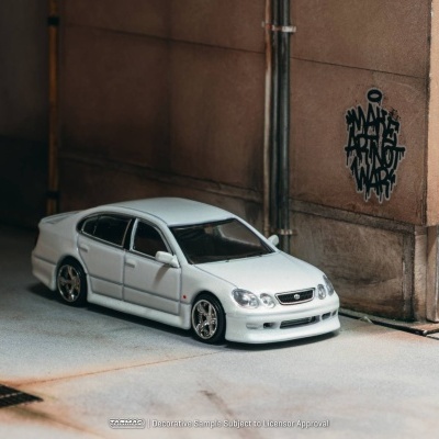 Miniatura de carro branco com grafiti numa parede castanha