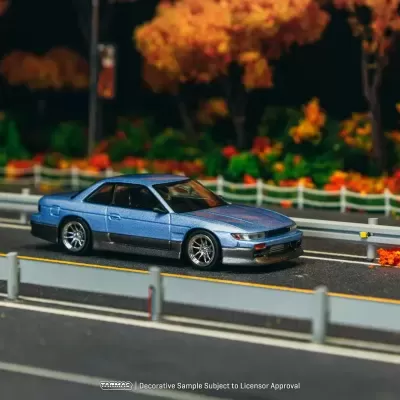 Miniatura de automóvel azul metálico numa estrada com árvores de outono ao fundo