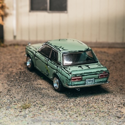 Miniatura de carro verde claro em superfície de cascalho junto a edifício.