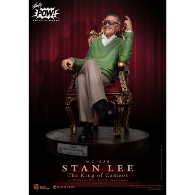 Figurina de Stan Lee sentado numa cadeira dourada com camisola verde e base preta.