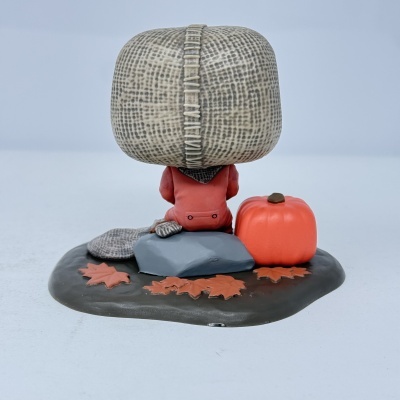 Figura decorativa de personagem sentado com abóbora e folhas de outono