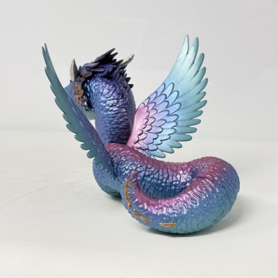 Figura de dragão colorido com escamas brilhantes e asas abertas sobre superfície branca