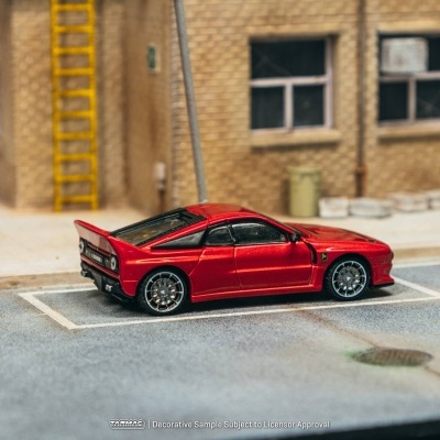 Miniatura de carro desportivo vermelho estacionado numa rua com paredes de tijolo amarelo