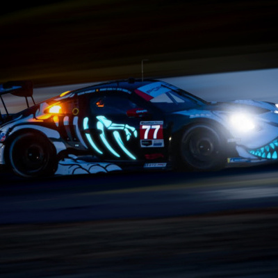 Carro de corrida preto com pintura luminosa azul e número 77 a correr à noite