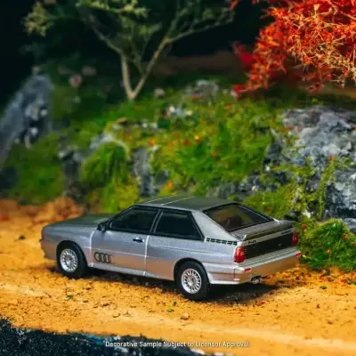 Miniatura de carro Audi cinza em cenário natural com terra e vegetação